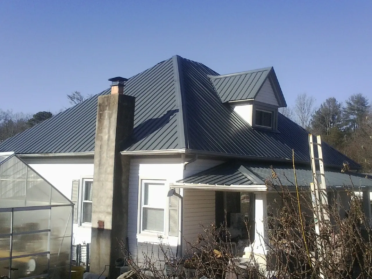 Dark blue standing seam metal roof on a white farmhouse with dormer — Slate & Tile Roof Repair by Roofing Brothers in Wildomar