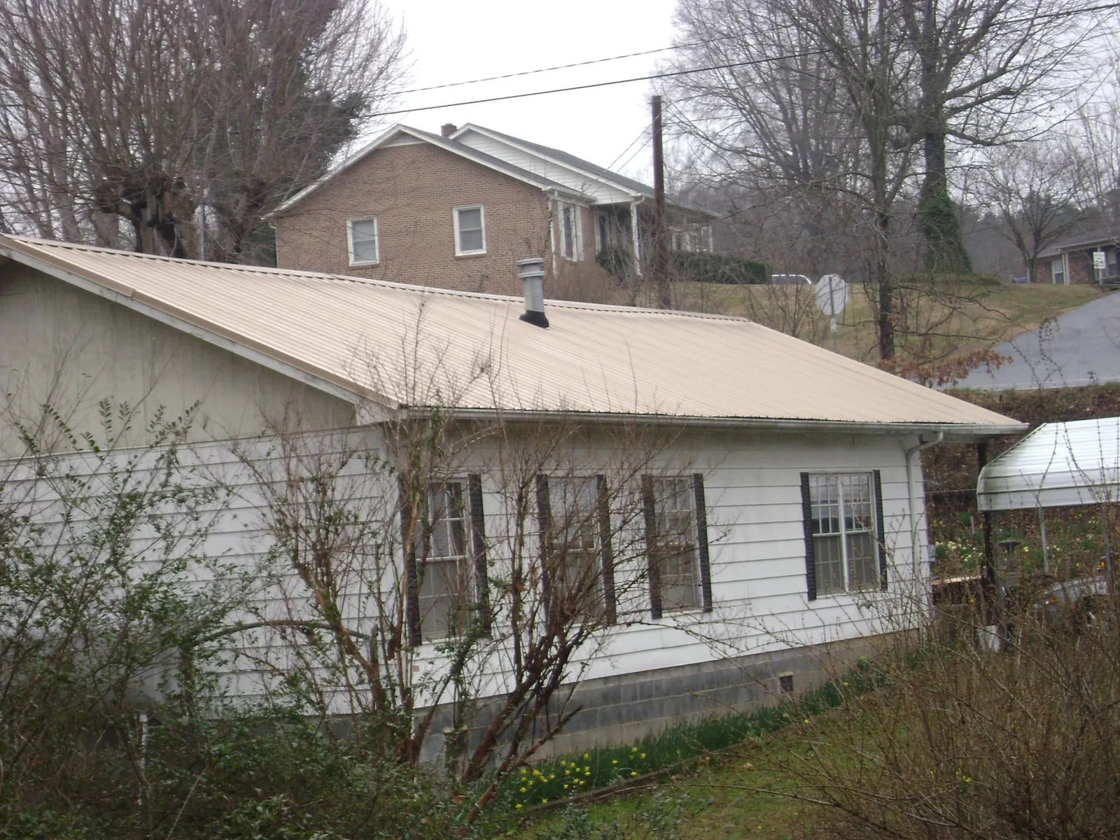 Tan metal roof on a white sided house set into a hillside — Commercial Roofing by Roofing Brothers in Wildomar